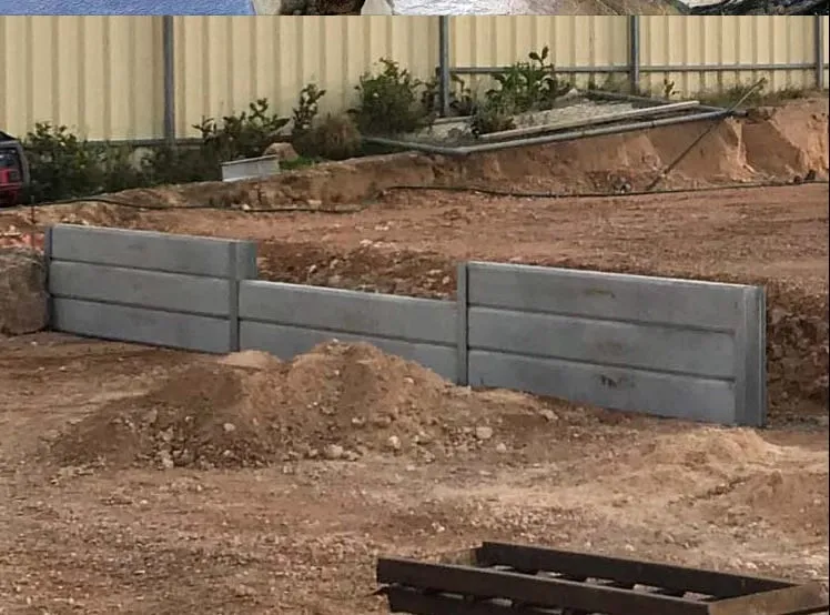 A concrete sleeper retaining wall part way through construction, with the posts set and the sleepers stacked behind them