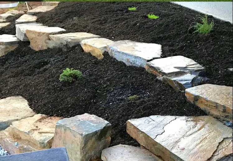 Stone slab steps and rock edging set into a black mulch garden bed
