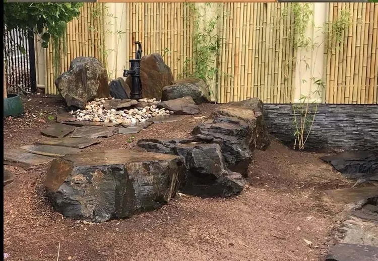 A rock water feature built against a bamboo screen